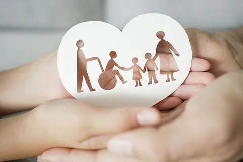 Hands holding a paper heart cut out in the shape of a family, including a person in a wheelchair
