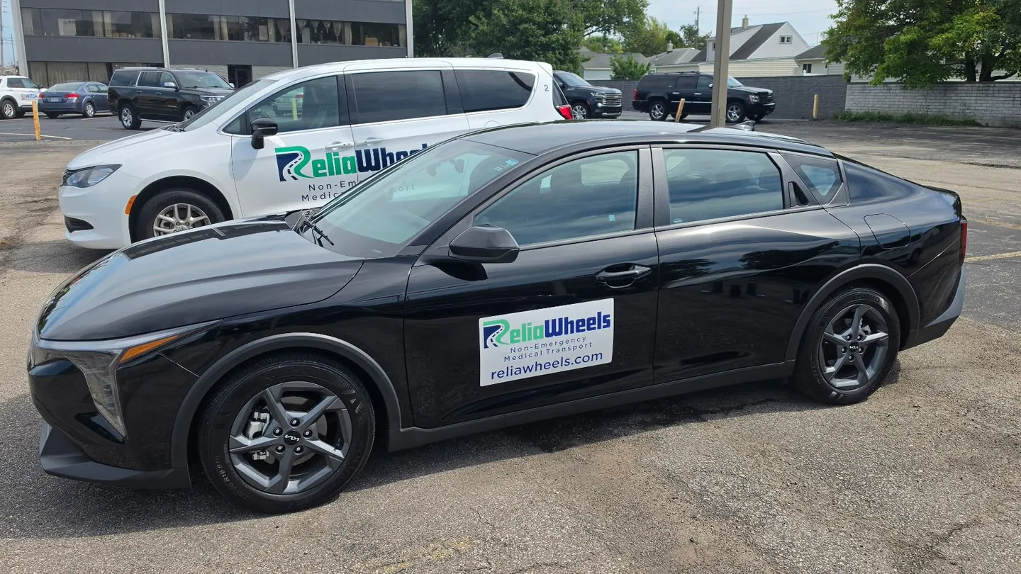 A black ReliaWheels sedan parked in front of a white ReliaWheels van