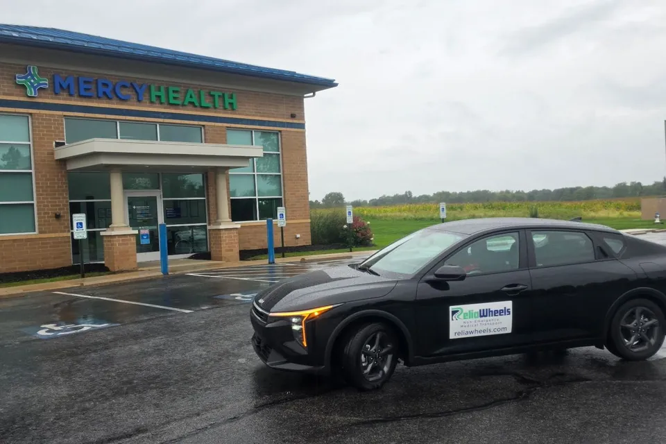 A black ReliaWheels sedan parked outside a Mercy Health medical building