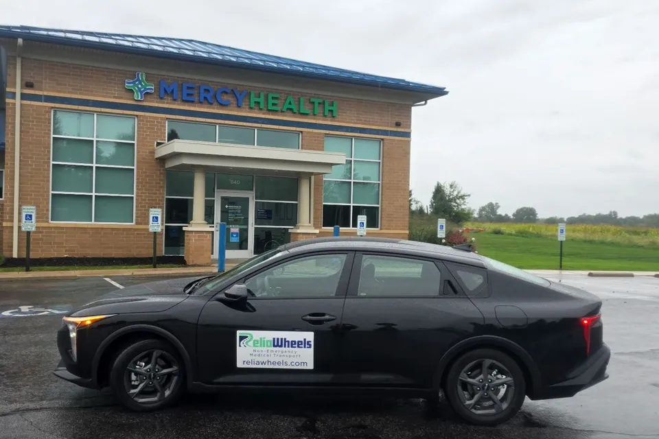 A black ReliaWheels sedan parked outside a Mercy Health medical building
