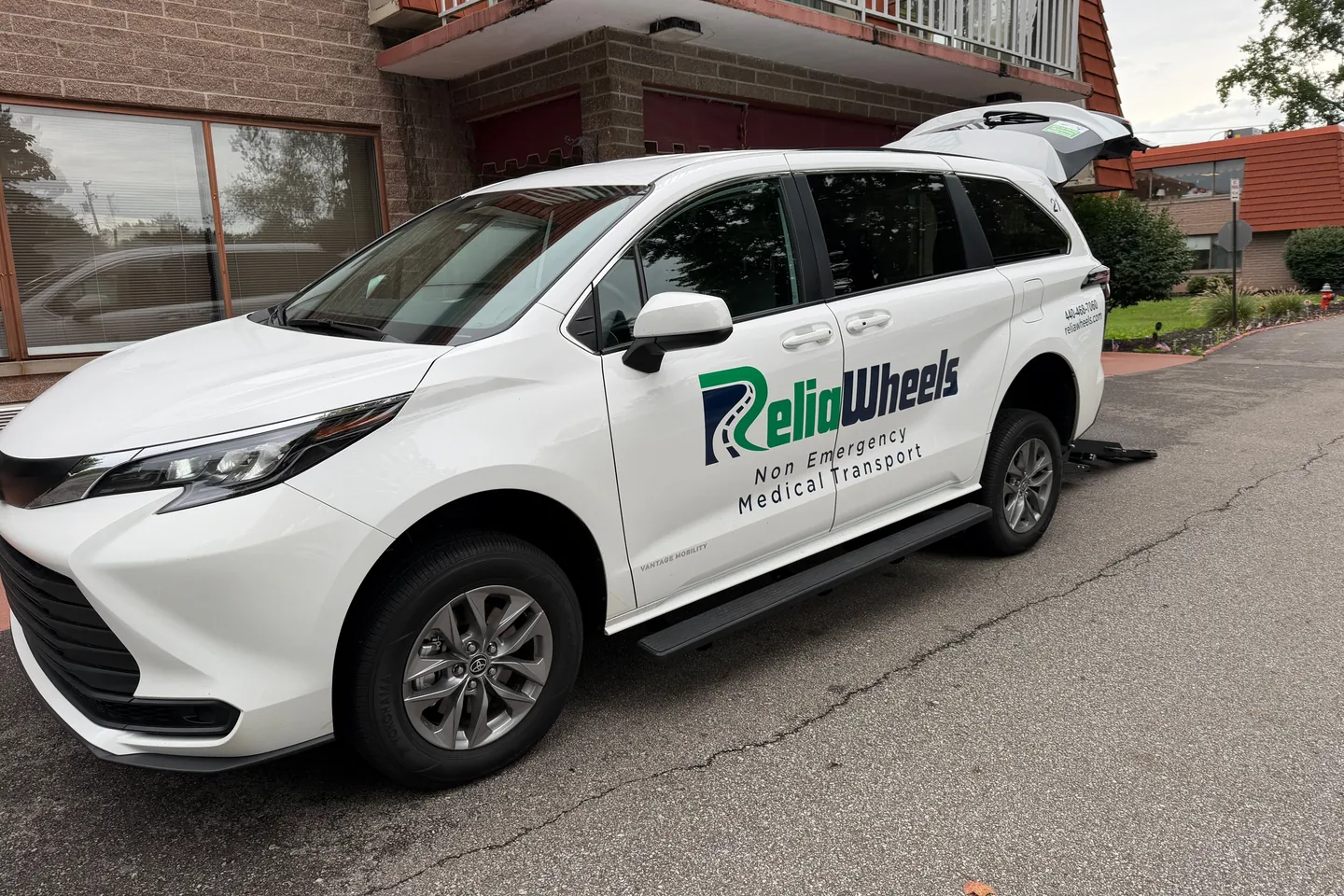 A white ReliaWheels wheelchair van parked outside a brick building