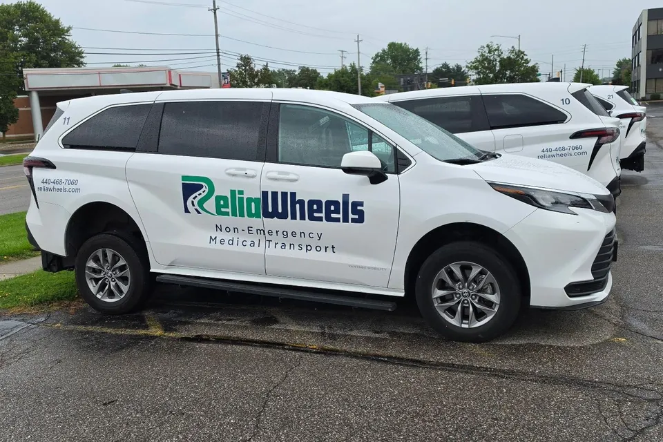 A white ReliaWheels wheelchair-accessible van parked in front of a row of matching vans