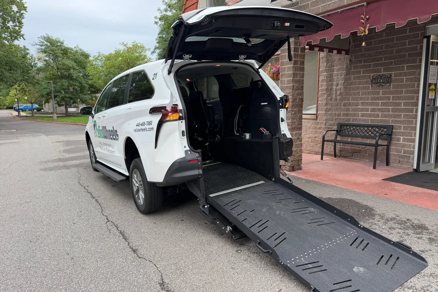 A ReliaWheels van parked outside a brick building with its rear door open and wheelchair ramp lowered to the pavement