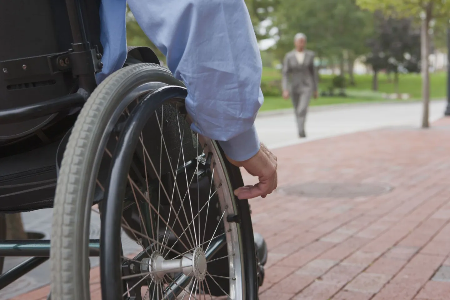 Close-up of a person's hand on the wheel of their wheelchair on a brick sidewalk